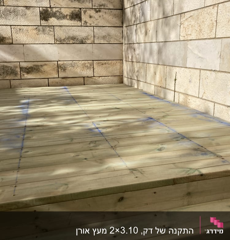 משטח עץ עם סימונים כחולים ליד קיר אבן